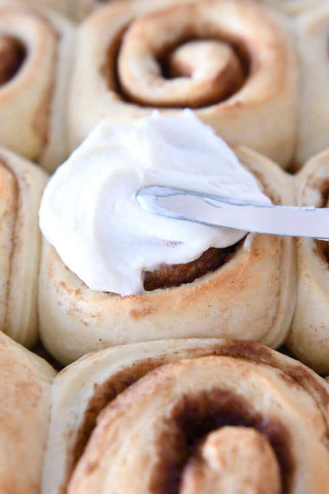Spreading frosting on baked cinnamon roll.