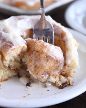 Fork digging out gooey center of cinnamon roll on white plate.