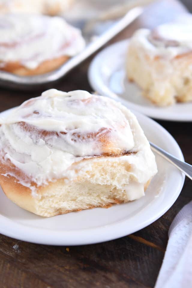 Baked cinnamon roll on white plate with fork.
