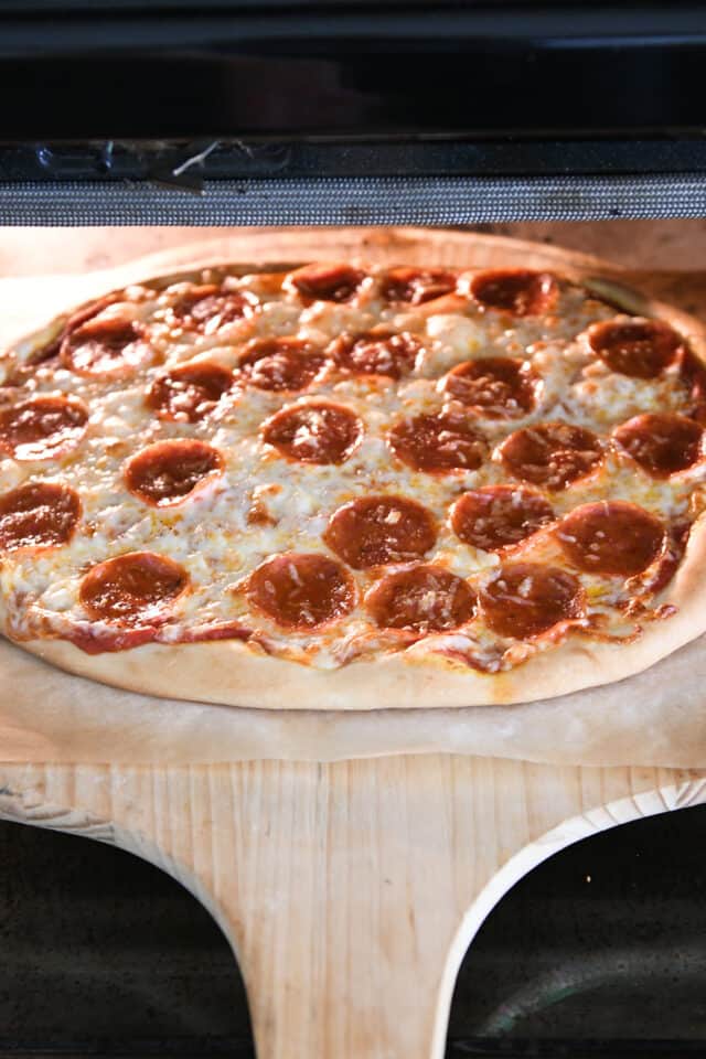 A baked pepperoni pizza taken out of the oven in a pizza crust.