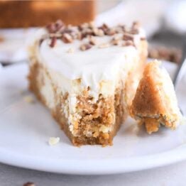 Slice of carrot cake cheesecake on white plate with fork.