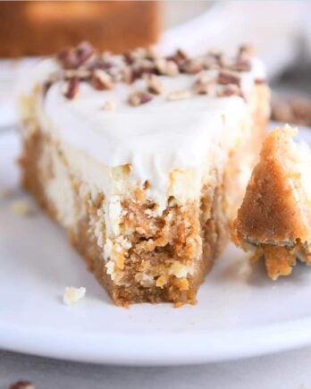 Slice of carrot cake cheesecake on white plate with fork.