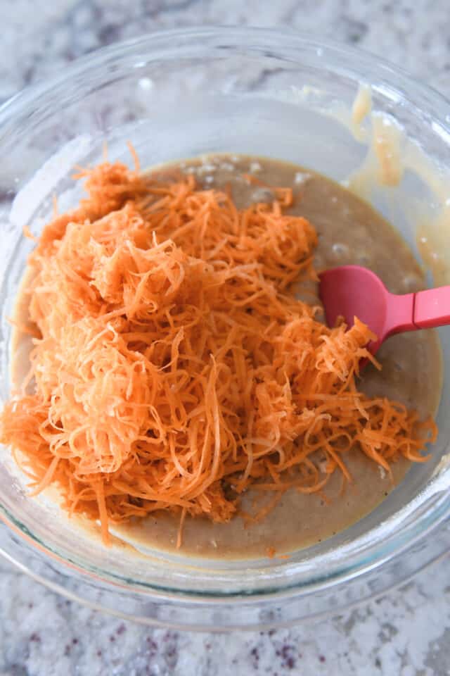 Shredded carrots in glass bowl with cake batter.