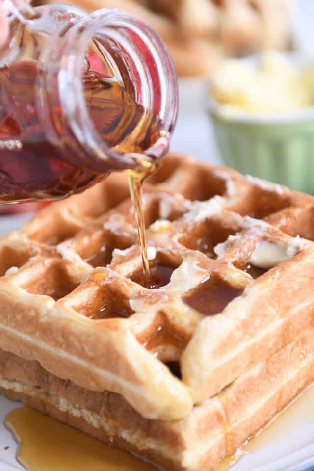 Pouring maple syrup on two stacked waffles.