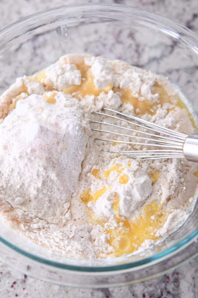 Whisking dry ingredients into waffle batter in glass bowl.