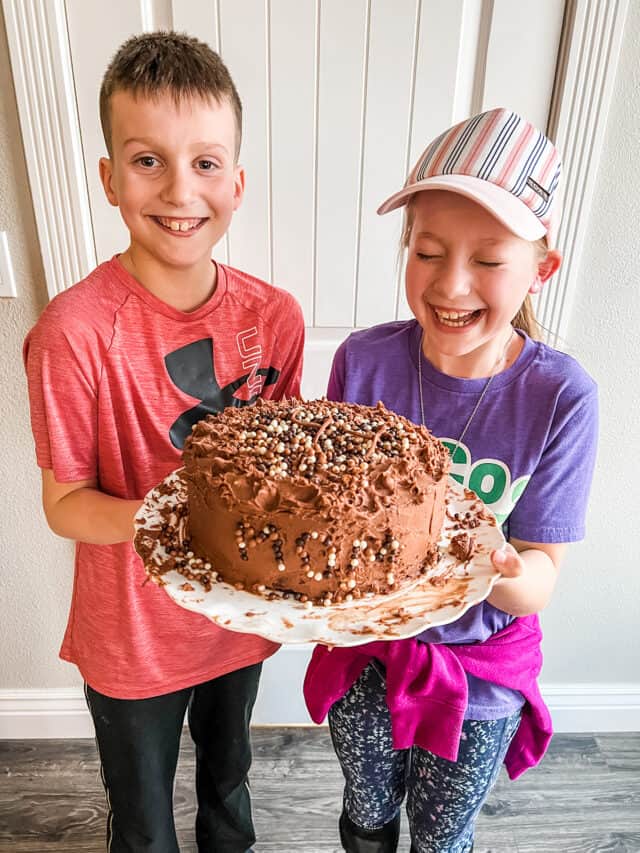 Two children laughing and holding a chocolate cake.