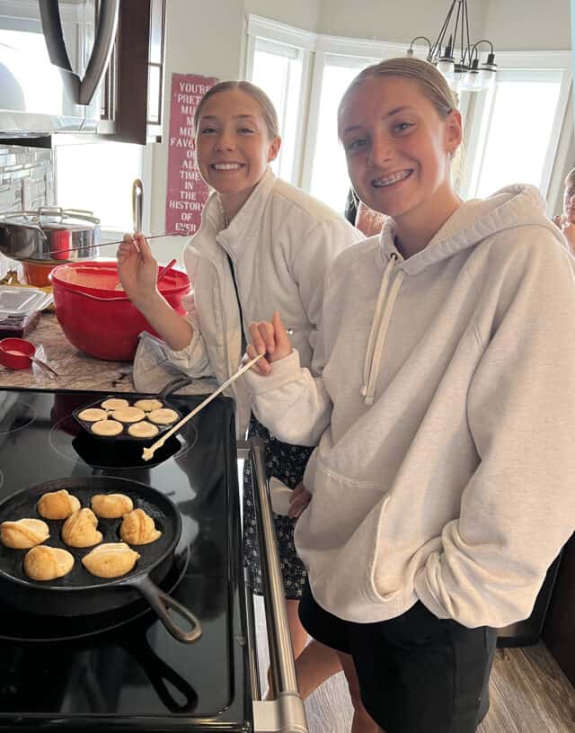 Two teenage girls cooking at the stove.