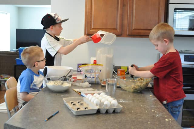 Young boys making cookies in messy kitchen.