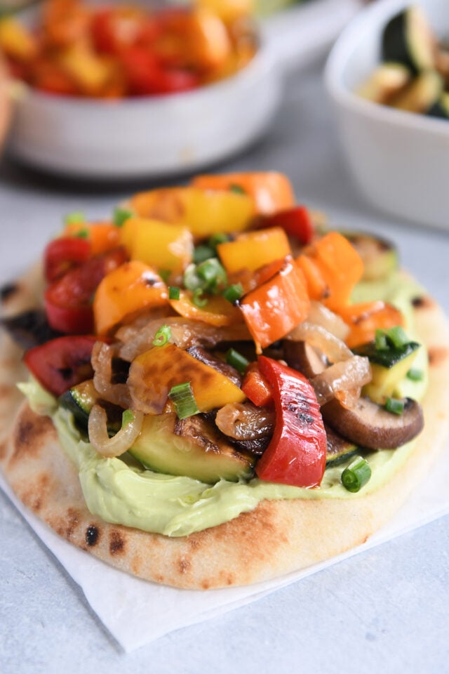 Flatbread on white parchment paper topped with creamy avocado sauce and roasted vegetables.