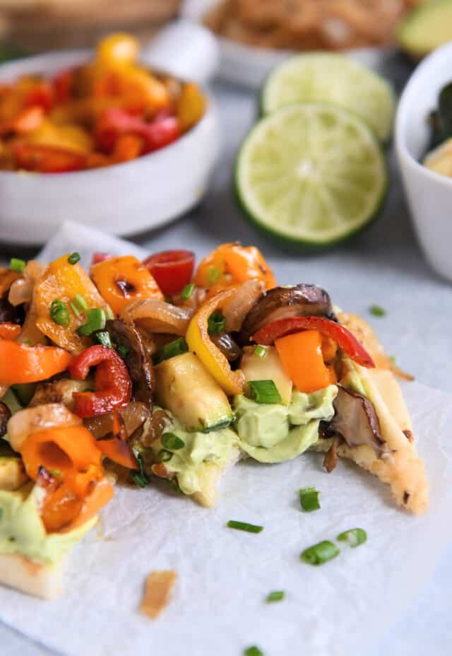 Bite taken out of flatbread with creamy avocado sauce and roasted vegetables.