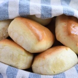 Five square rolls in basket with blue and white towel.