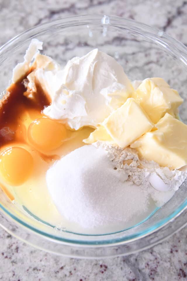 Butter, flour, sugar, eggs, vanilla, sour cream, and baking powder in glass bowl.