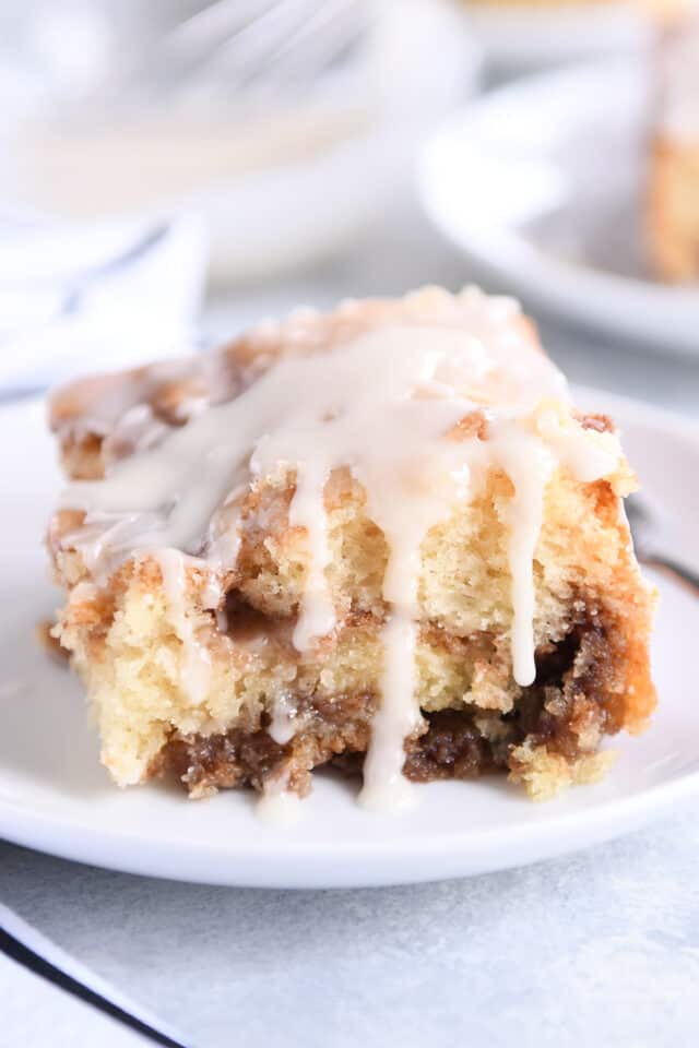 Square of cinnamon cake with glaze drizzling down sides.