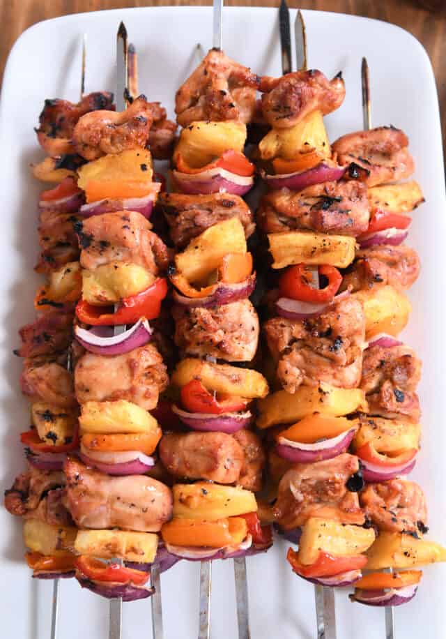 Five metal skewers with pieces of chicken, pineapple, onions and peppers.