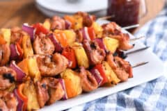 Several chicken, pineapple and pepper skewers on metal sticks on white platter.