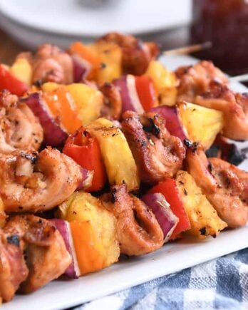 Several chicken, pineapple and pepper skewers on metal sticks on white platter.