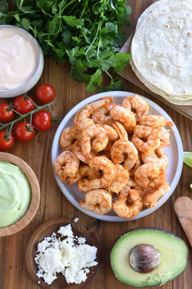A plate of shrimp, cherry tomatoes, avocado sauce, tortillas, coriander and cotiha cheese.