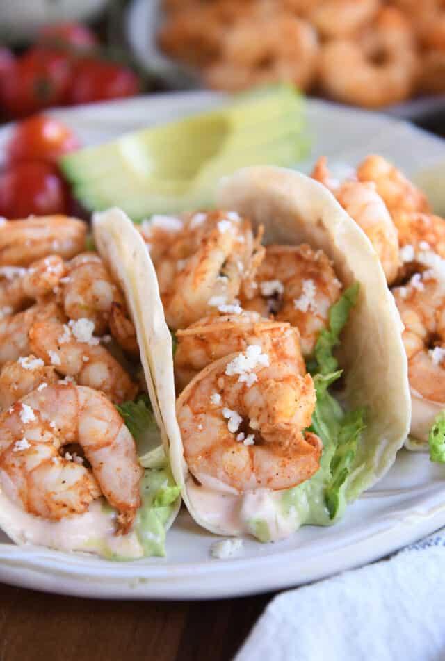 Three shrimp tacos on white ridged plate.