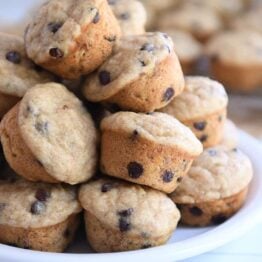 Stack of mini banana chocolate chip muffins on white plate.