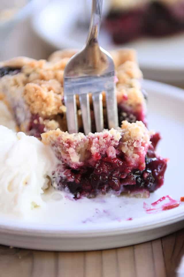 Fork taking bite of triple berry rhubarb pie with ice cream.