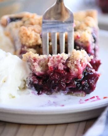 Fork taking bite of berry rhubarb pie and vanilla ice cream on gray plate.