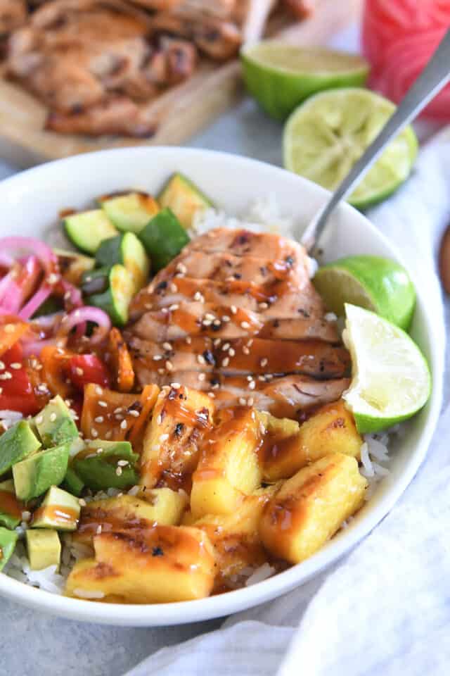 White bowl with slices of grilled chicken, fresh limes, pineapple, avocados, peppers and zucchini.