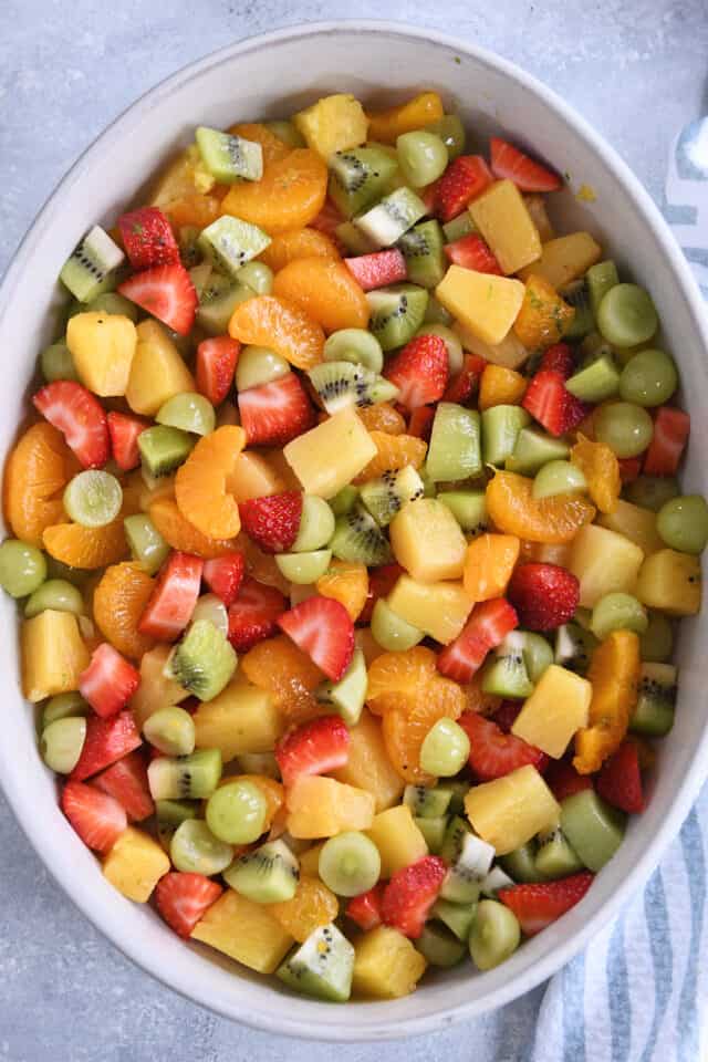 White oval serving dish filled with strawberries, mandarin oranges, pineapple and kiwi.