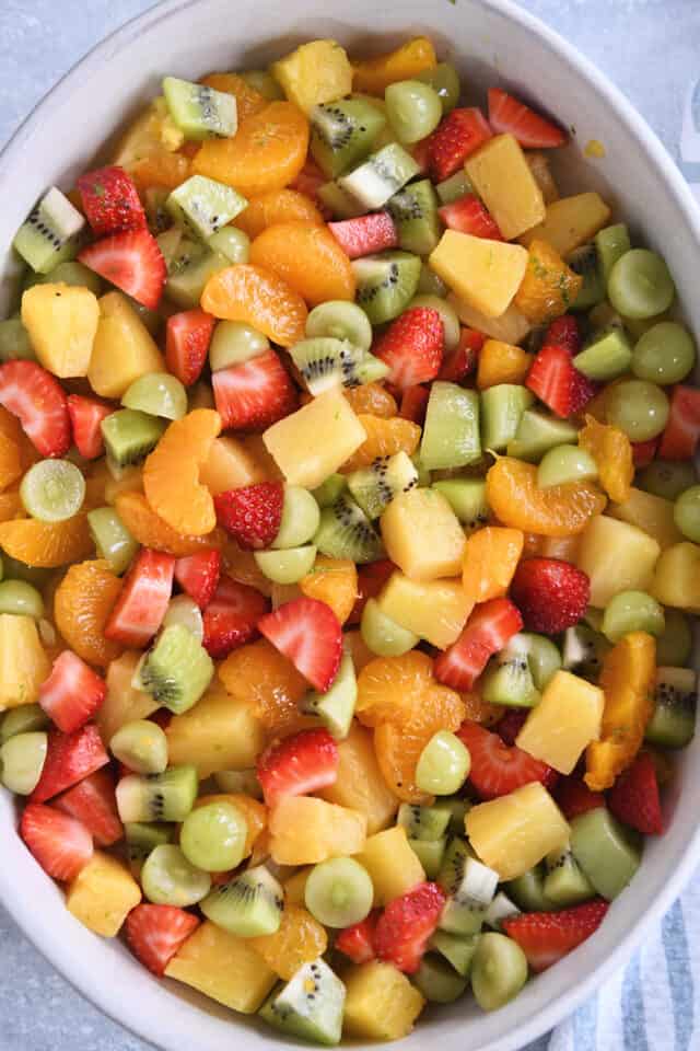 White oval serving dish with canned pineapple, strawberries, grapes, and kiwi.