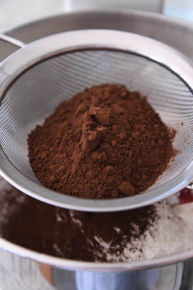 Sifting cocoa into bowl with cookie batter.