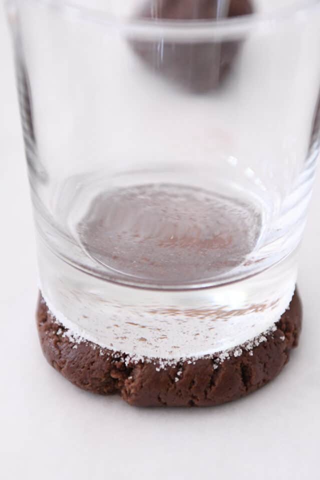 Pressing cookie dough ball flat with glass.