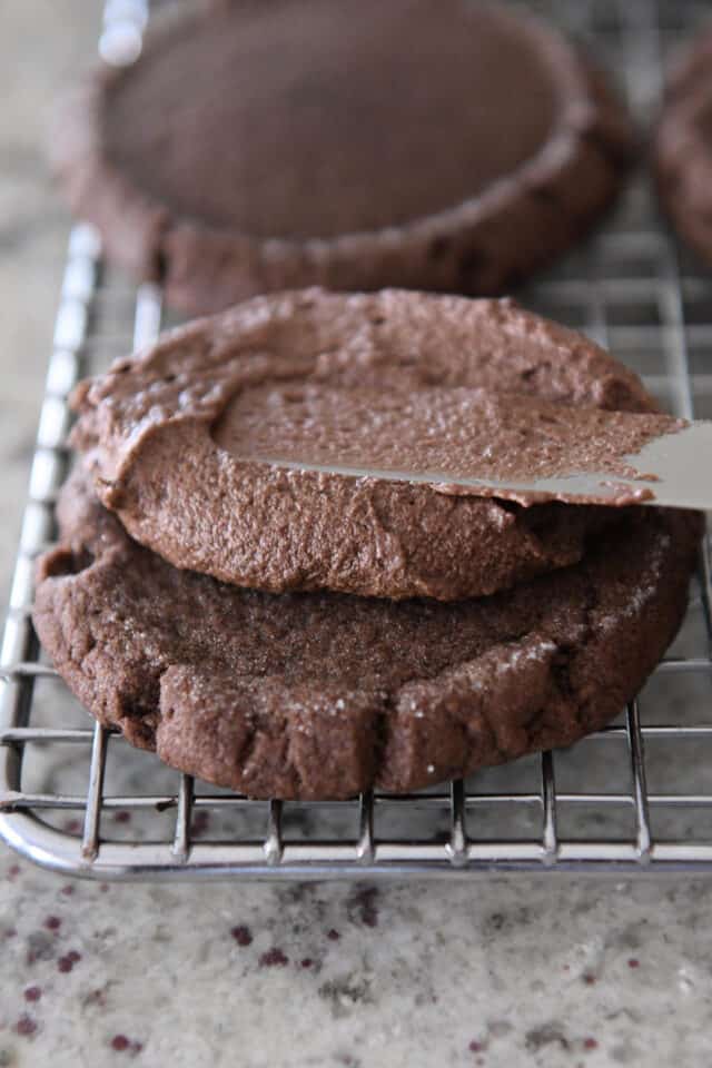 Spreading chocolate frosting on chocolate cookie.