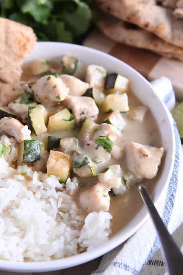 White bowl with white rice and chicken and zucchini in coconut lime sauce.