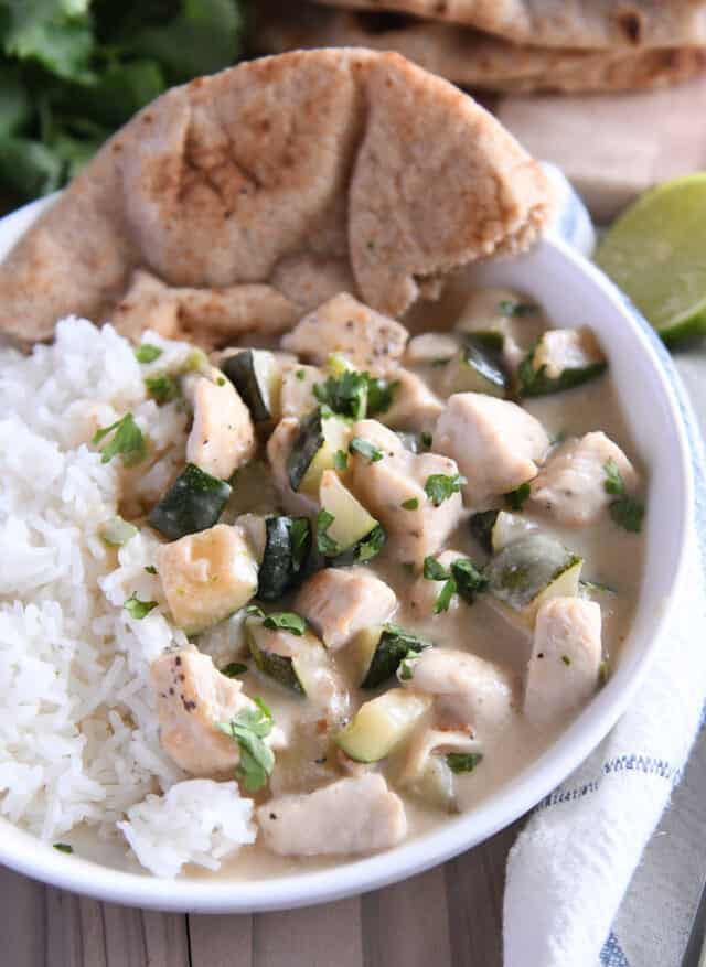 White bowl with pieces of chicken and zucchini in cream sauce over white rice.