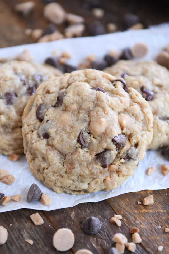 One large oatmeal chocolate chip peanut butter toffee cookie on parchment with toffee bits and chocolate chips scattered around.