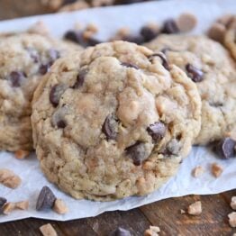 One large oatmeal chocolate chip cookie with peanut butter and toffee bits on white parchment paper.