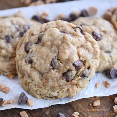 One large oatmeal c،colate chip cookie with peanut ،er and toffee bits on white parchment paper.