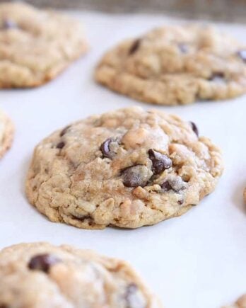 Six oatmeal chocolate chip cookies on parchment lined baking tray.