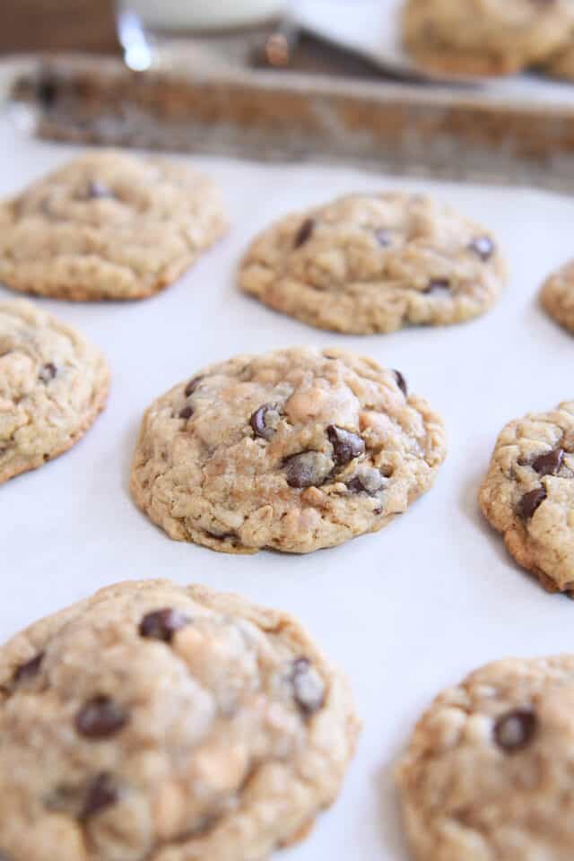 Five or six large oatmeal c،colate chip cookies with peanut ،er and toffee on parchment lined baking tray.