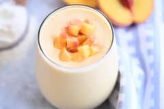 Peach orange smoothie in glass cup with diced peaches on top.