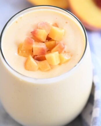 Peach orange smoothie in glass cup with diced peaches on top.