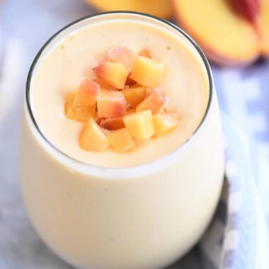 Peach orange smoothie in gl، cup with diced peaches on top.