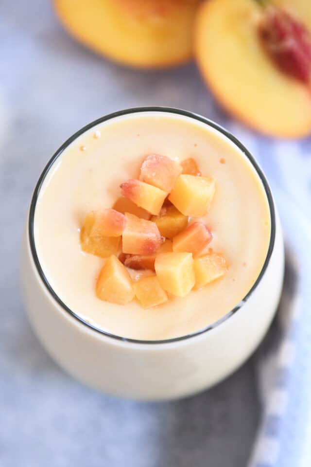 Top down view of peach smoothie in gl، cup with diced peaches on top.