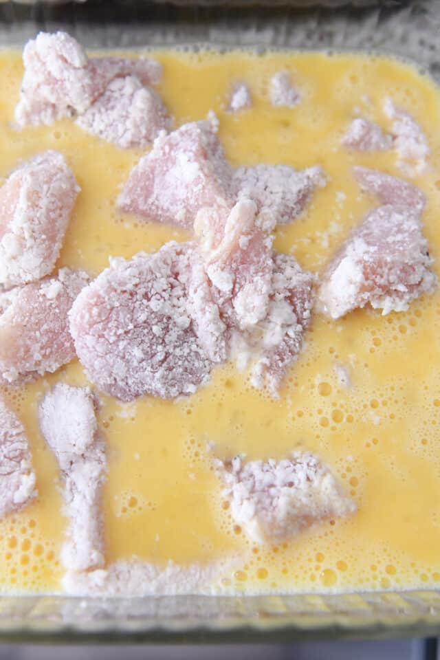 Chicken pieces coated in cornstarch sitting in a whisked egg mixture.
