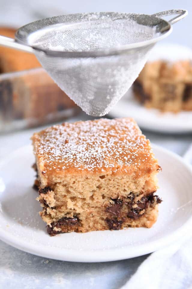 Dusting top of square piece of cake with powdered sugar.