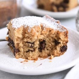 Half eaten square of chocolate chip cake dusted with powdered sugar on white plate.