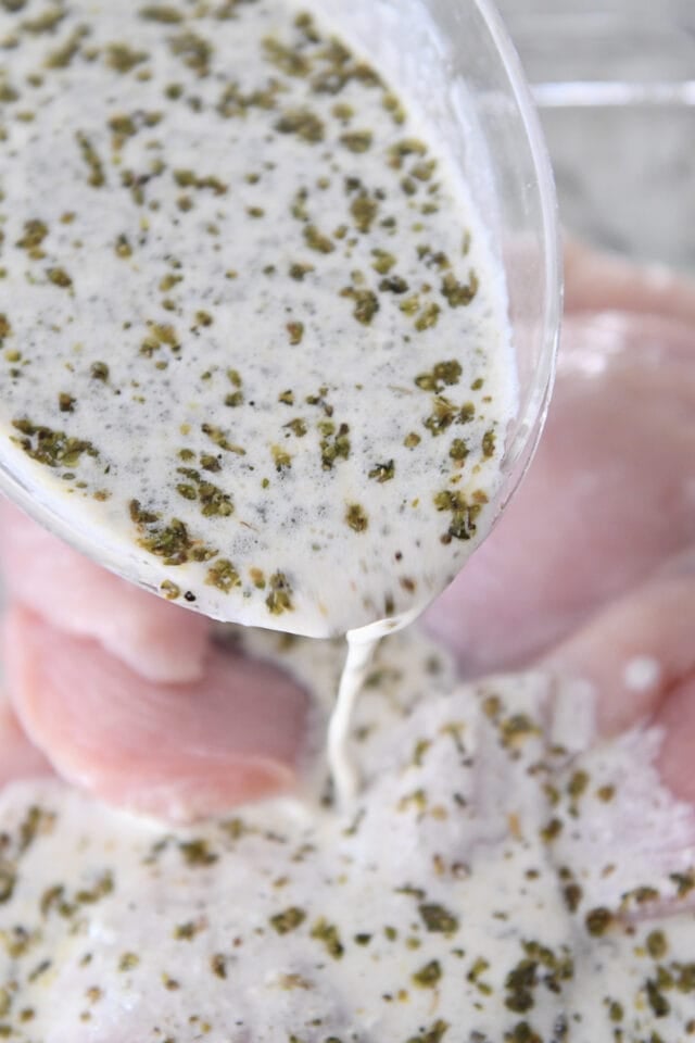 Pouring yogurt marinade over chicken.