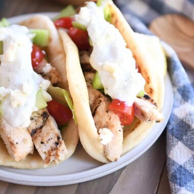 Two chicken gyros in flatbread with tzatziki, tomatoes and lettuce on gray plate.