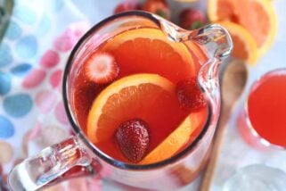 Top down view of red punch in glass pitcher with sliced oranges and strawberries.