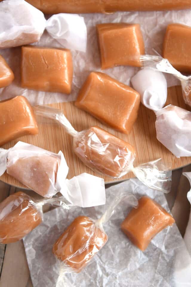 Unwrapped caramels next to wrapped caramels in cellophane and parchment paper.