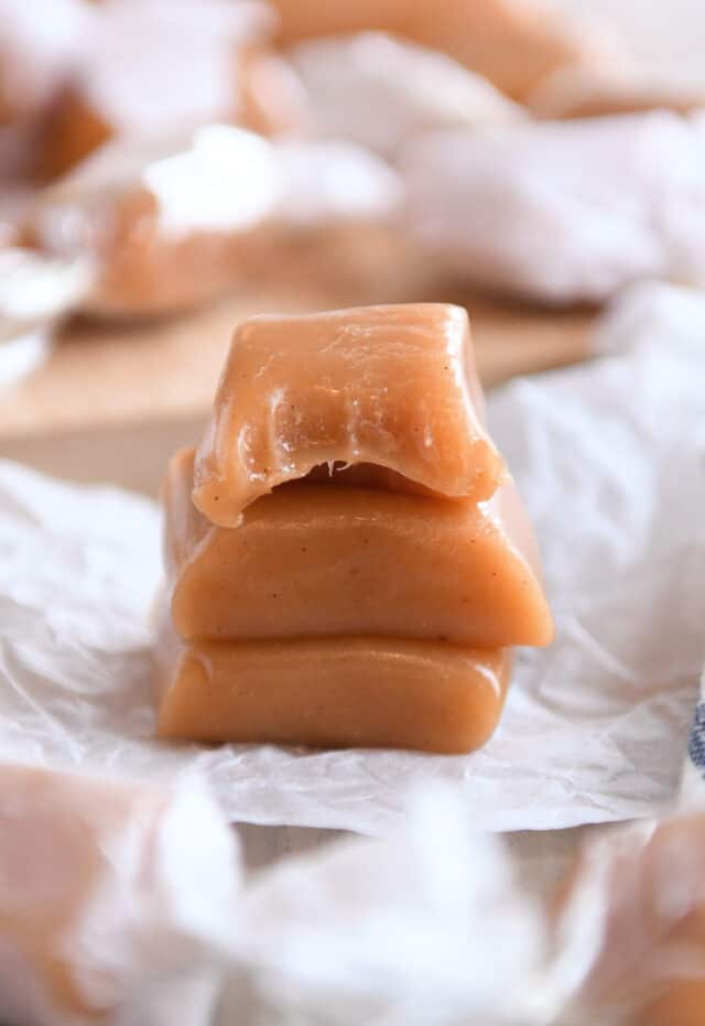 Three apple cider caramels stacked with the top caramel bitten in half.